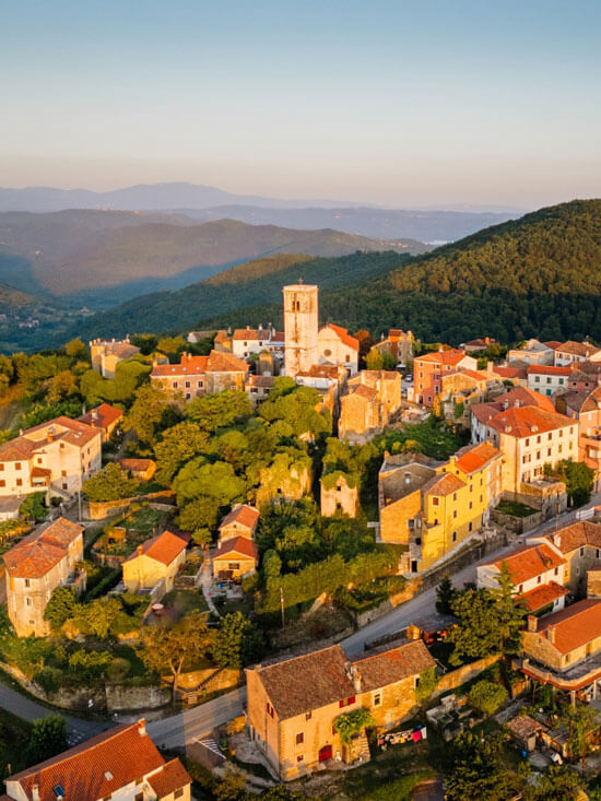 Aerial golden hour view of Grožnjan with church bell tower and surrounding green hills